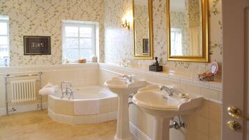A bathroom with a large bathtub, two sinks, a large mirror, and floral wallpaper.