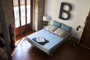 Un dormitorio con una cama, una lámpara, una decoración grande en forma de 'B' en la pared y suelo de madera.
