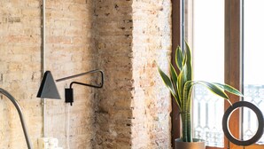 A bedroom with a brick wall, a wooden dresser, a potted plant, a bed, a lamp, and a window with a view. - Bubuflats Mossen (Valencia)