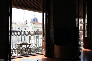 Una habitación con piso de madera, una pequeña mesa con un cuenco y una planta, y vista a edificios con una estructura en forma de cúpula.