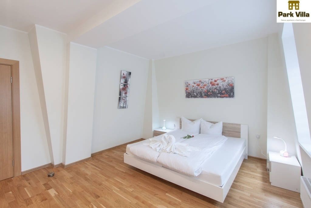Een moderne slaapkamer met een groot bed, een houten vloer, een witte deur en een schilderij aan de muur.