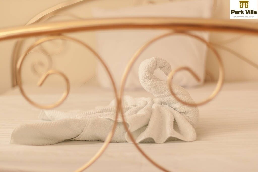 A neatly folded white towel on a bed with a gold metal headboard.