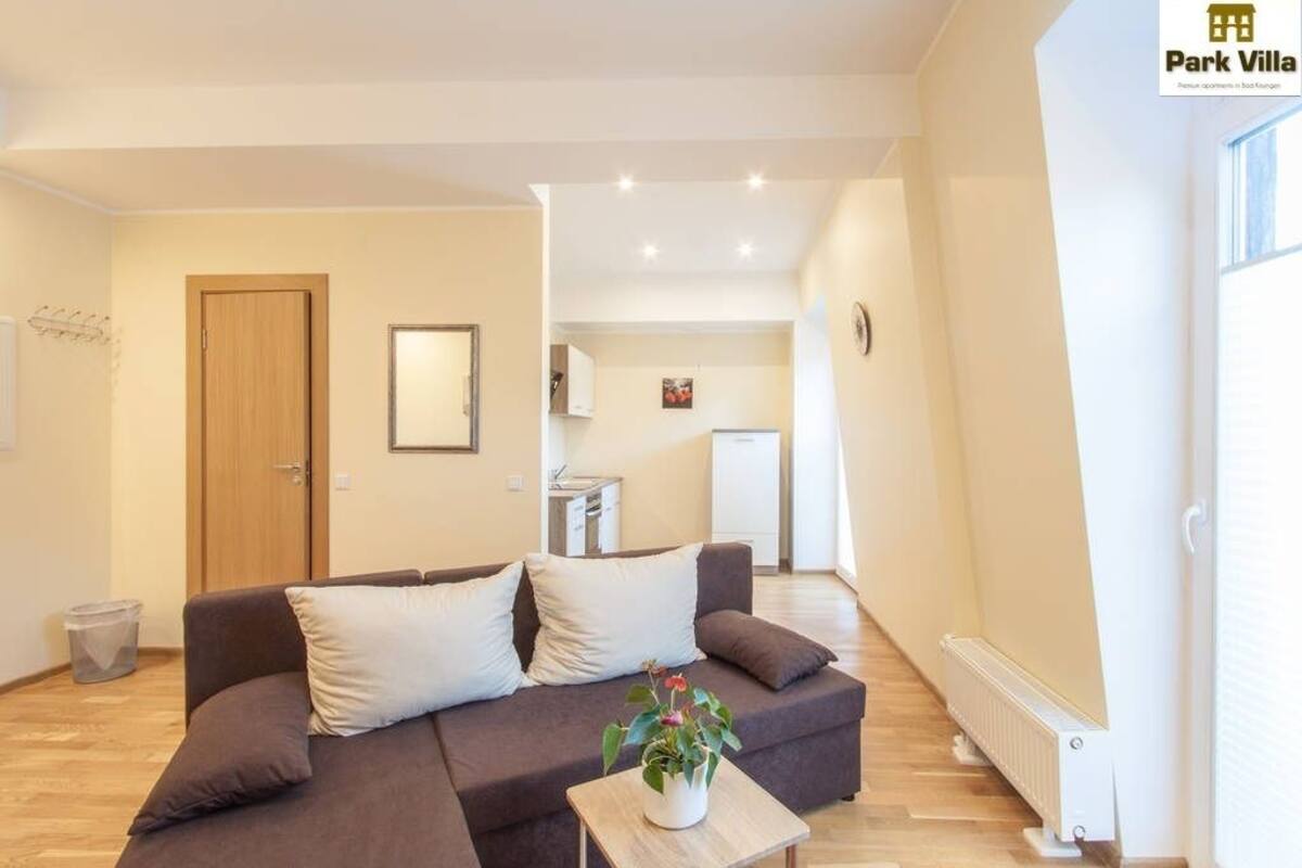 Een moderne woonkamer met een bank, een kleine tafel met een plant en een keuken op de achtergrond.