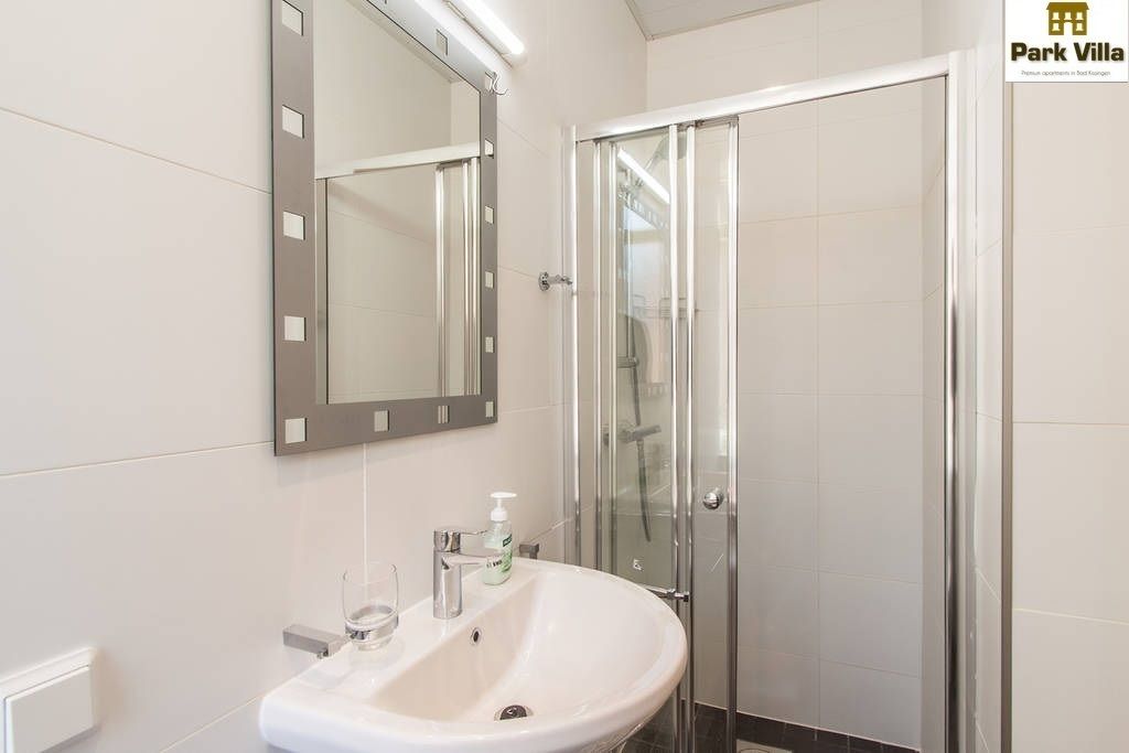 Une salle de bain moderne avec un lavabo blanc, un miroir et une cabine de douche en verre.