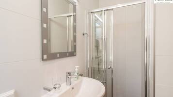 Une salle de bain moderne avec un lavabo blanc, un miroir et une cabine de douche en verre.
