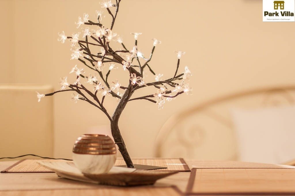 A small indoor tree with white flowers in a bowl on a wooden table.