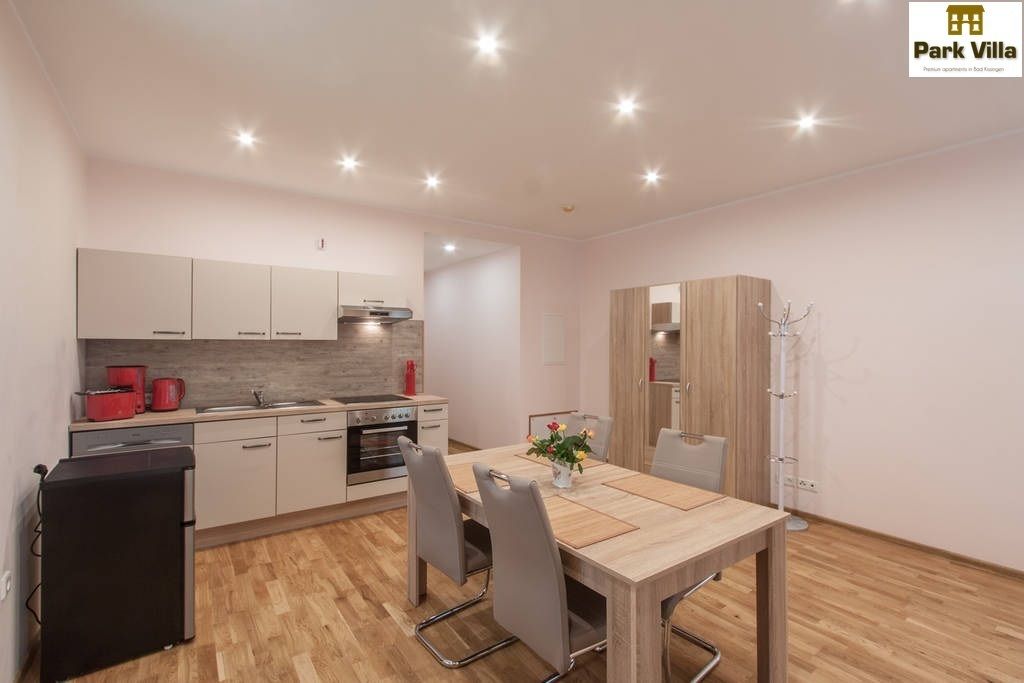 A modern kitchen with white cabinets, a black refrigerator, and a wooden dining table with chairs.