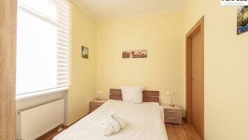 A bedroom with a bed, bedside tables, a radiator, and a window with blinds.