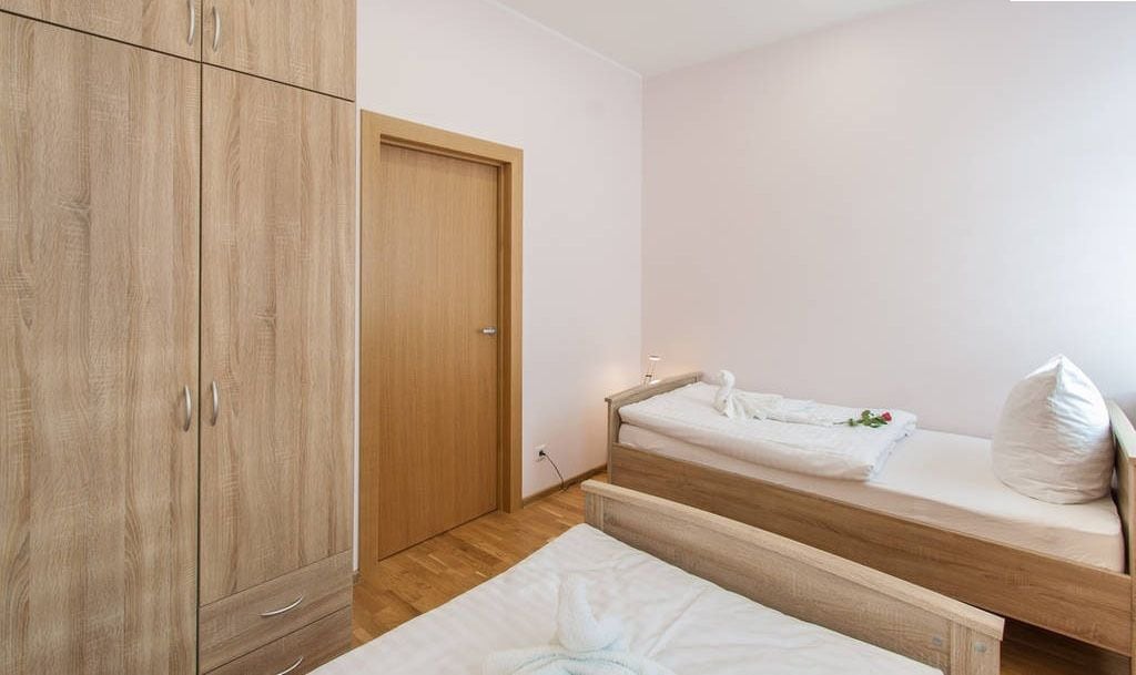 Een slaapkamer met een houten garderobe, een enkel bed met wit beddengoed en een klein nachtkastje.