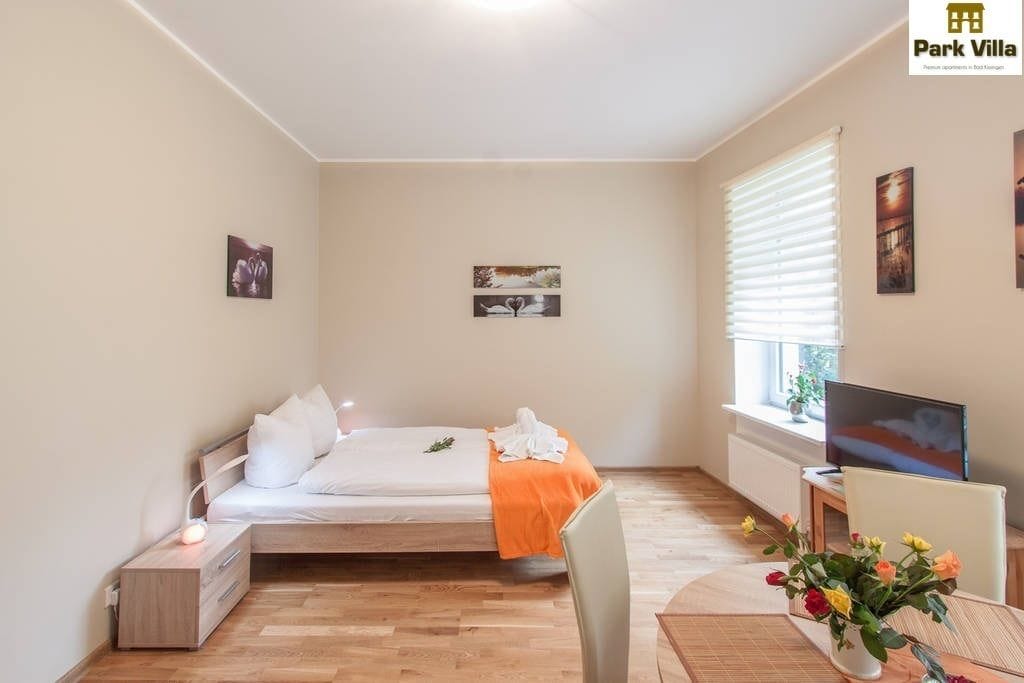 Ein Schlafzimmer mit Bett, Nachttisch, Fernseher und einem Fenster mit Jalousien.