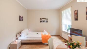 A bedroom with a bed, bedside table, TV, and a window with blinds.