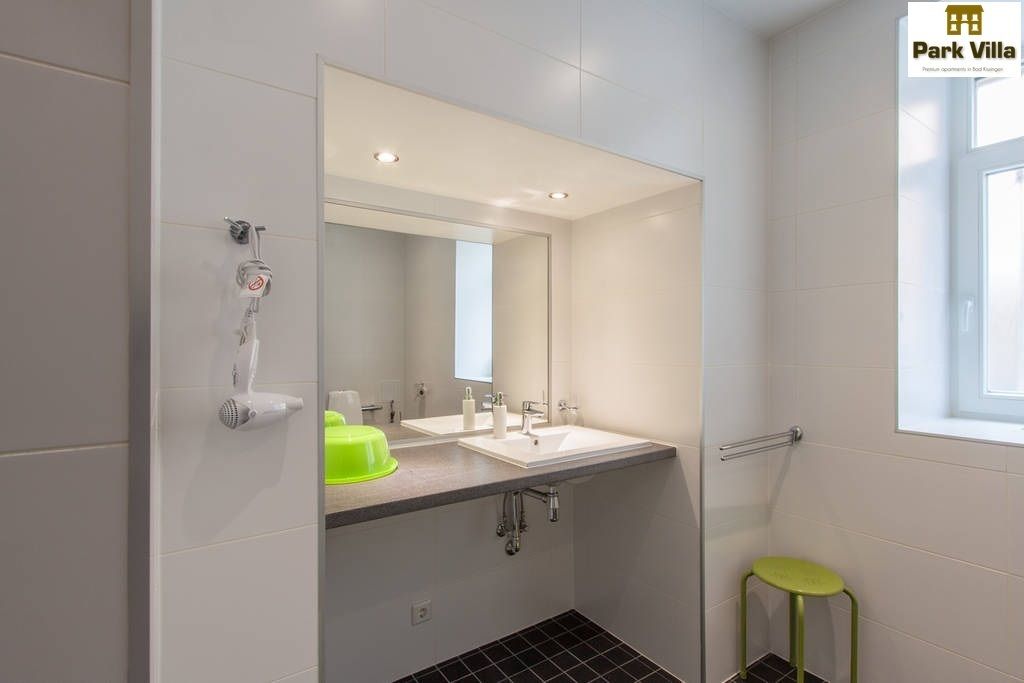 Un baño moderno con dos lavamanos, un espejo, una ducha y un taburete verde.