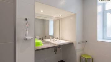 Un baño moderno con dos lavamanos, un espejo, una ducha y un taburete verde.