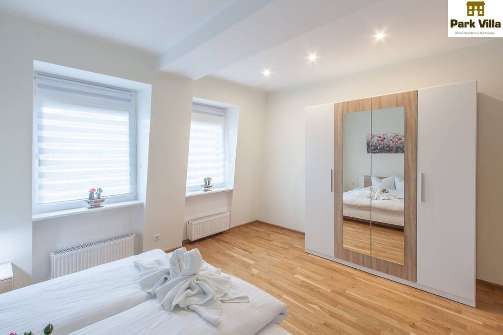 Un dormitorio con cama, armario y dos ventanas con persianas.