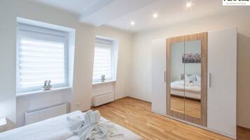 Un dormitorio con cama, armario y dos ventanas con persianas.