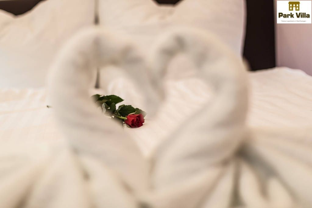A bed with a heart-shaped towel arrangement and a single red rose.