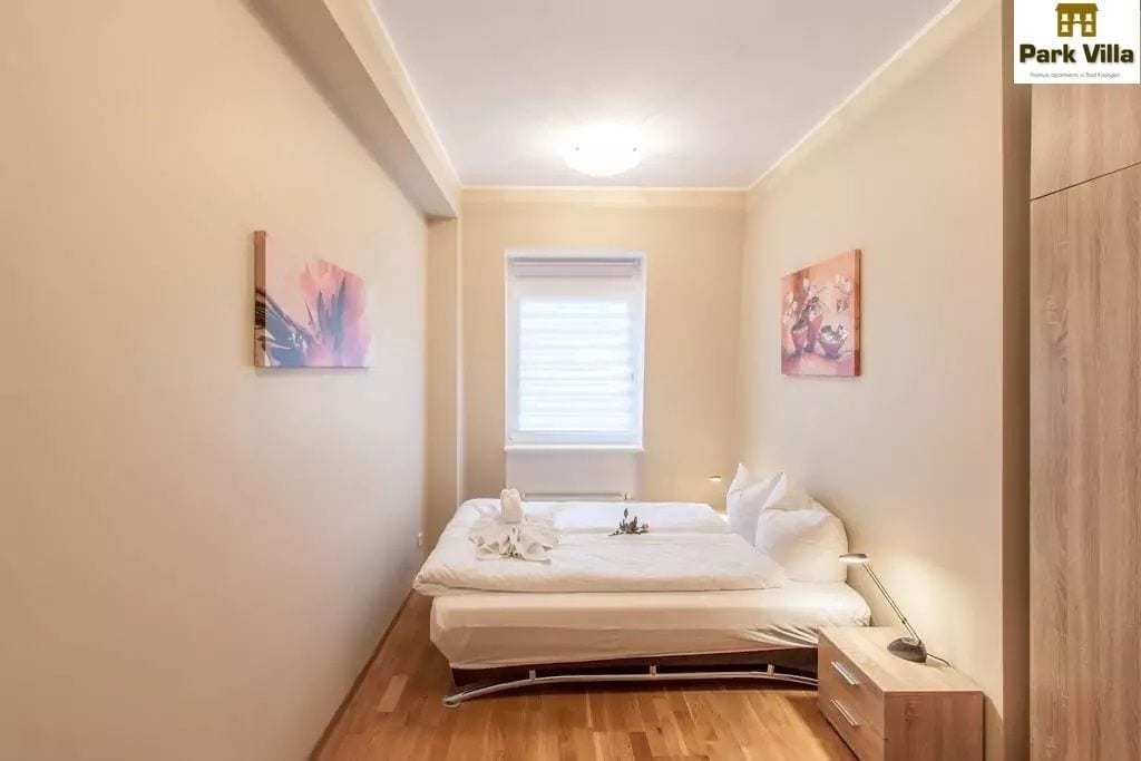 A small, modern bedroom with a bed, bedside tables, and artwork on the walls.
