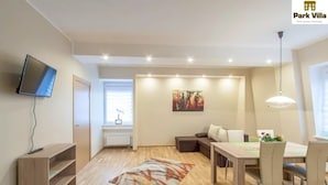 Una sala moderna con un televisor de pantalla plana, una mesa de comedor con sillas, un sofá y un cuadro en la pared.
