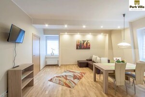 Una sala moderna con un televisor de pantalla plana, una mesa de comedor con sillas, un sofá y un cuadro en la pared.