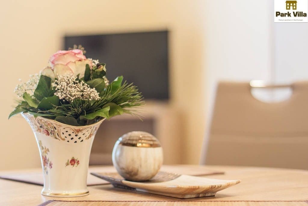 Un vase blanc orné de motifs floraux, une rose rose et des feuilles vertes sur une table en bois.