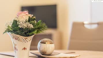 Un vase blanc orné de motifs floraux, une rose rose et des feuilles vertes sur une table en bois.
