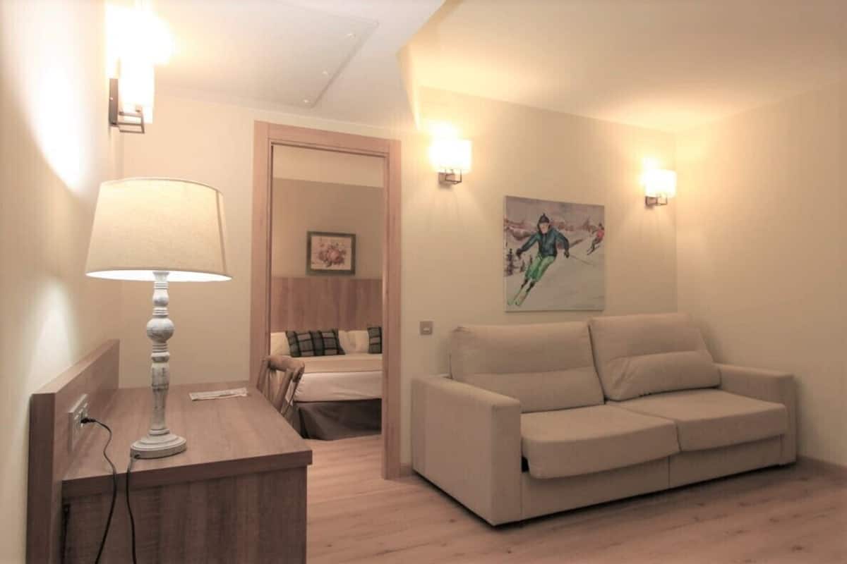 A hotel room with a wooden desk, a lamp, a beige sofa, and a painting on the wall.