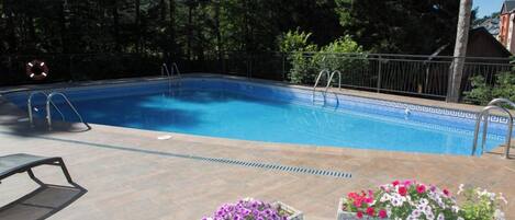 Una piscina con escalones, rodeada por una terraza de madera y macetas de piedra con flores.
