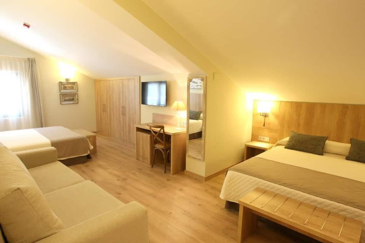 A hotel room with a bed, two sofas, a desk, a chair, a TV, and a mirror.