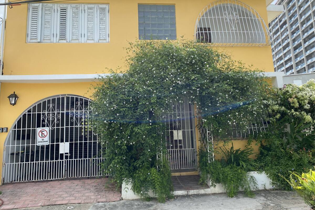A yellow building with barred gates, a no parking sign, and a tree in front.
