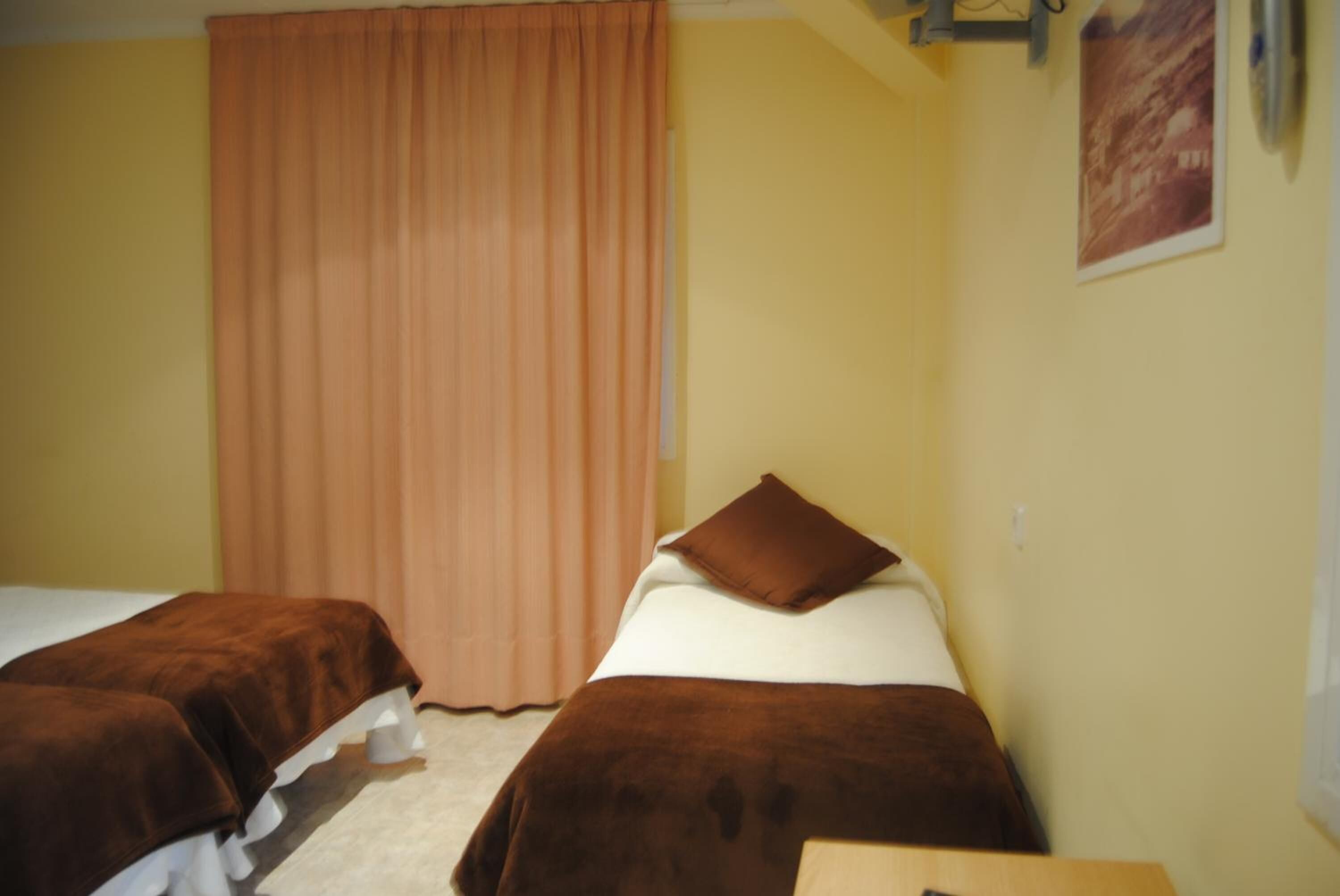 A room with two beds, a window with curtains, and a wall-mounted light fixture.