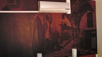 Habitación con un mural que representa una calle de pueblo antiguo, un aire acondicionado blanco y un escritorio de madera con una silla.