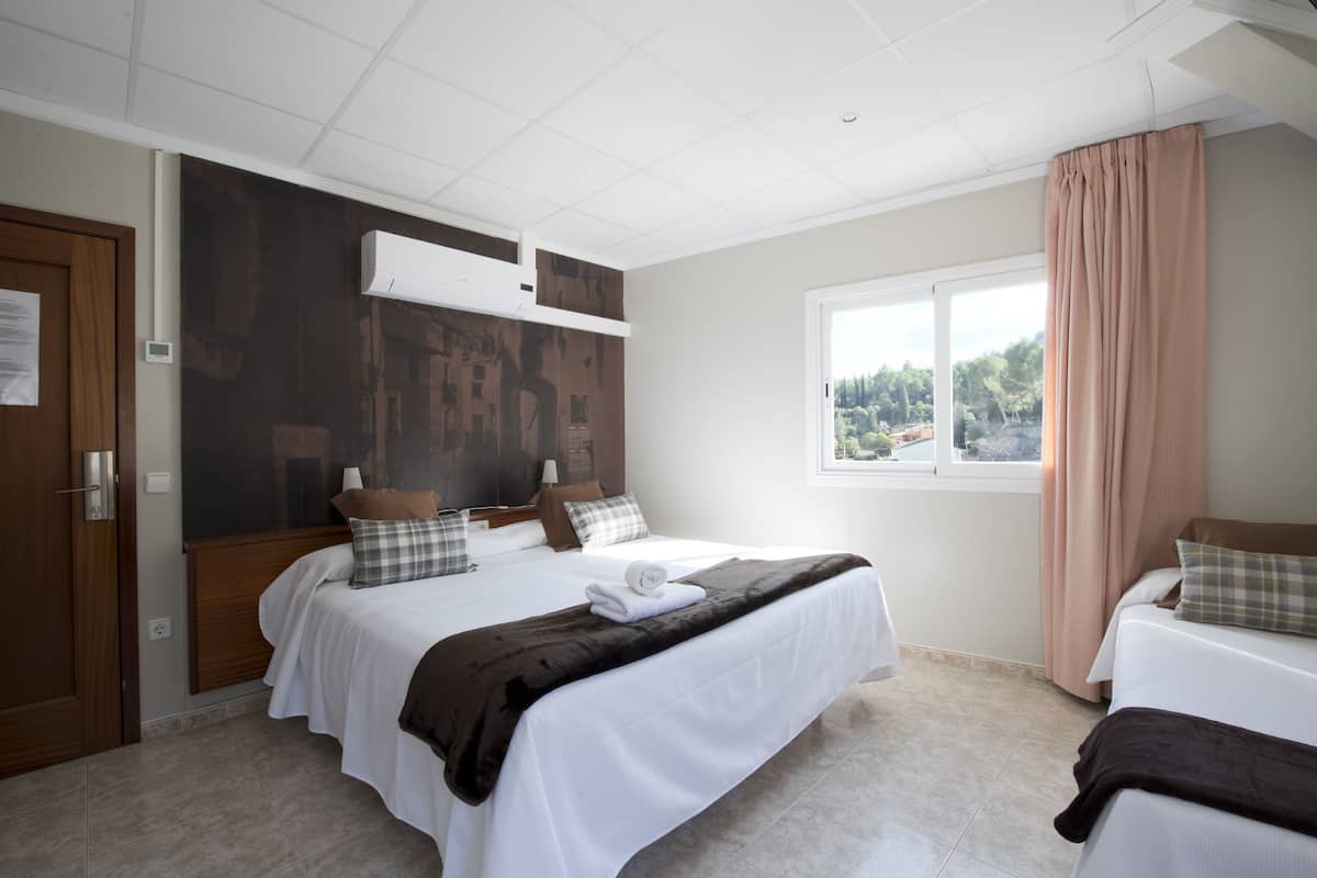 Una habitación de hotel con una cama grande, una mesita de noche, una ventana con cortinas y un cabecero de madera.