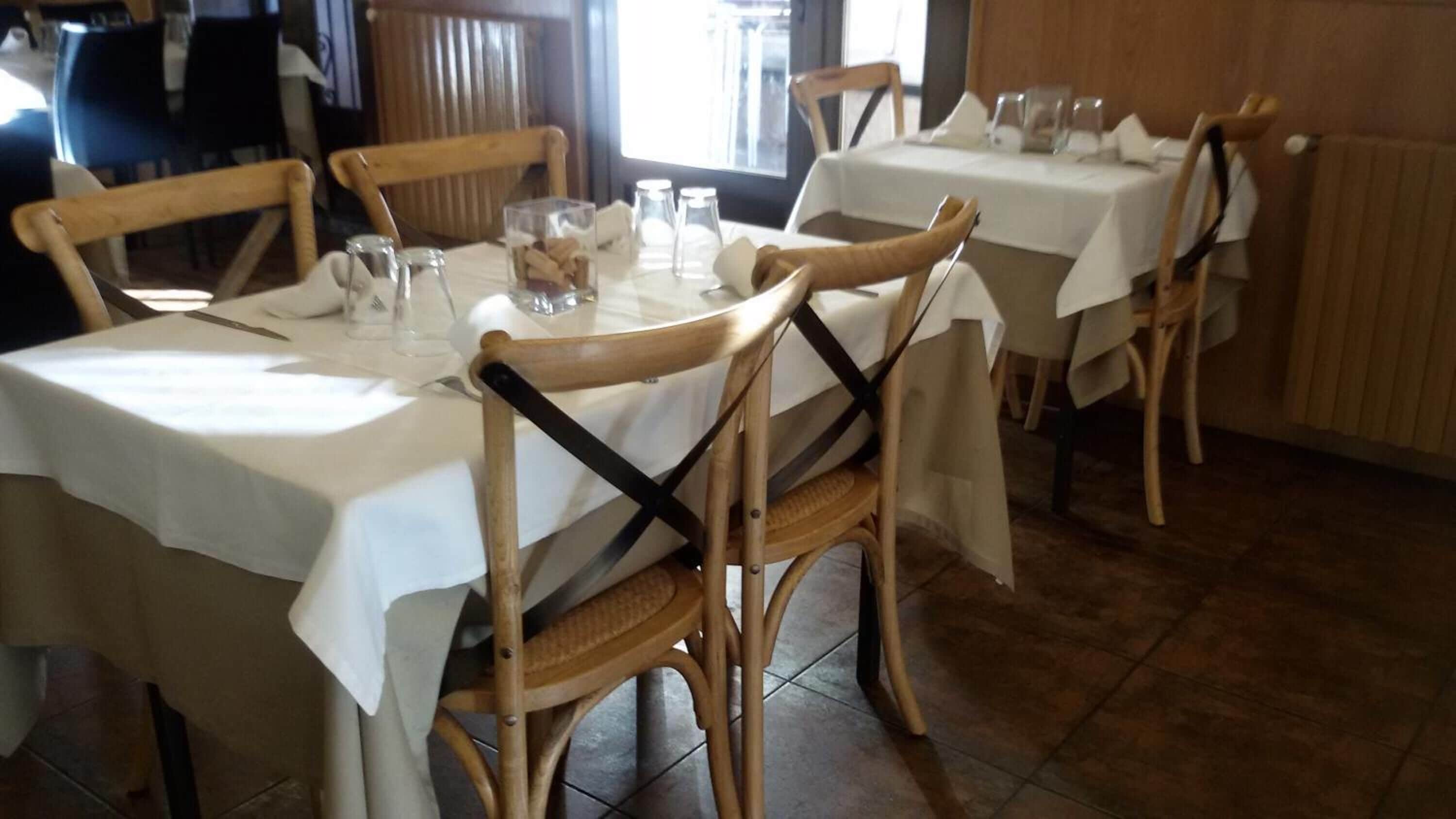 A dining area with round tables covered with white tablecloths, wooden chairs, and clear glassware.