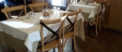 A dining area with round tables covered with white tablecloths, wooden chairs, and clear glassware.