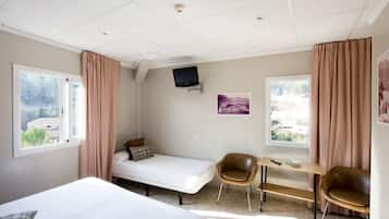 Una habitación con cama, escritorio, silla, televisor y ventana con cortinas.