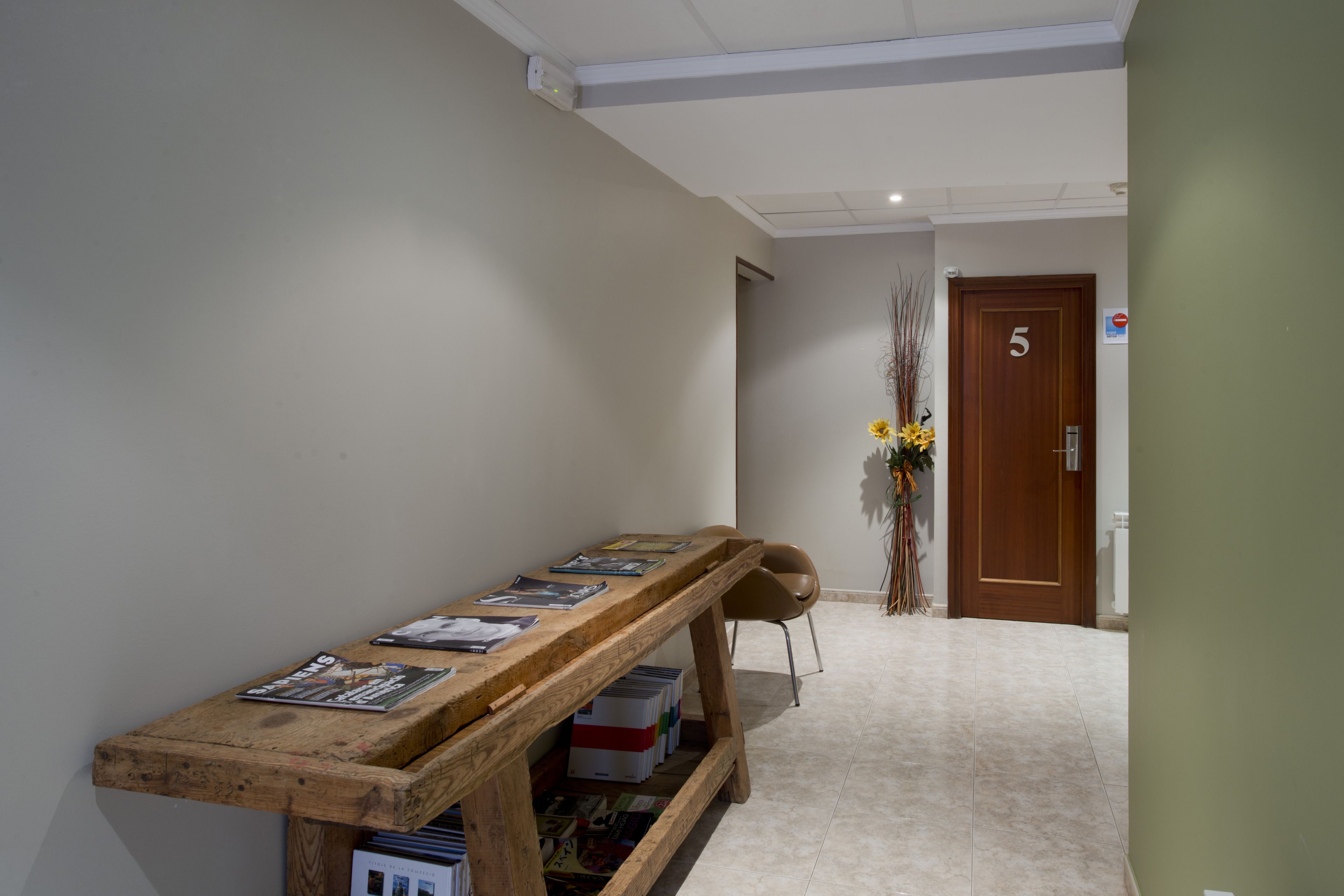 A hallway with a wooden bench displaying magazines, a door labeled '5', and a vase with flowers.