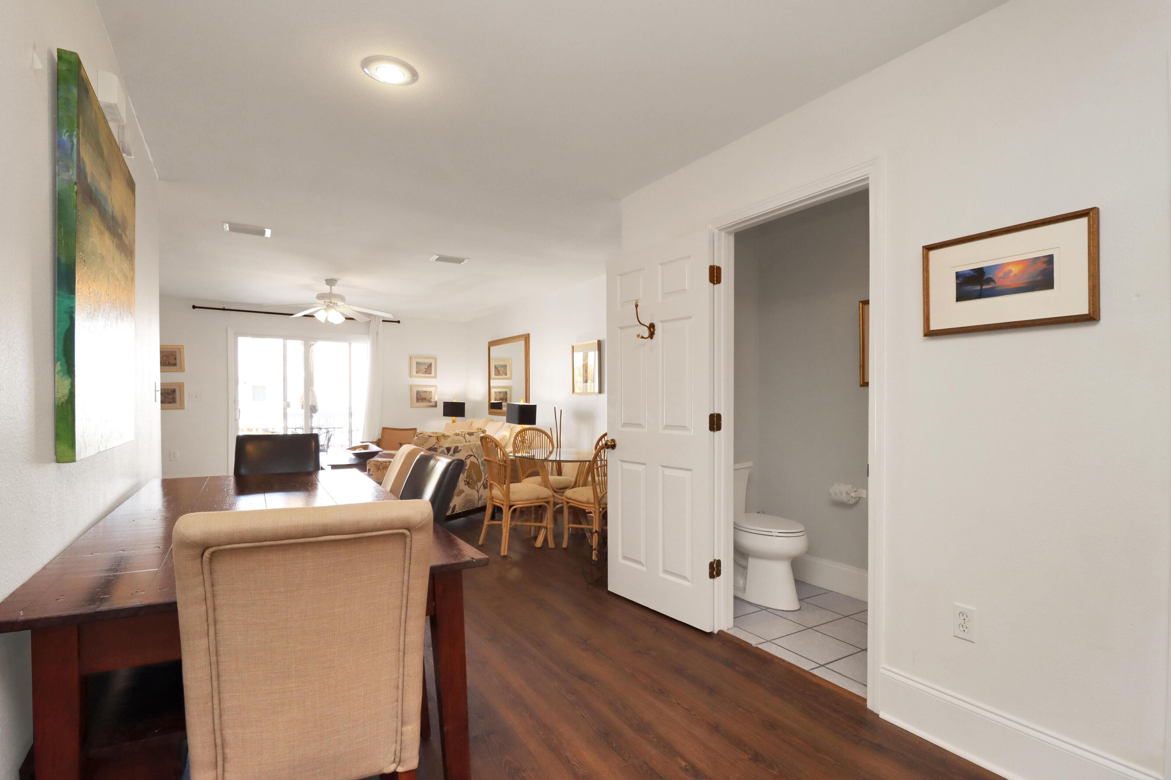 A spacious living room with a dining area, a ceiling fan, and a view into the adjacent bathroom.