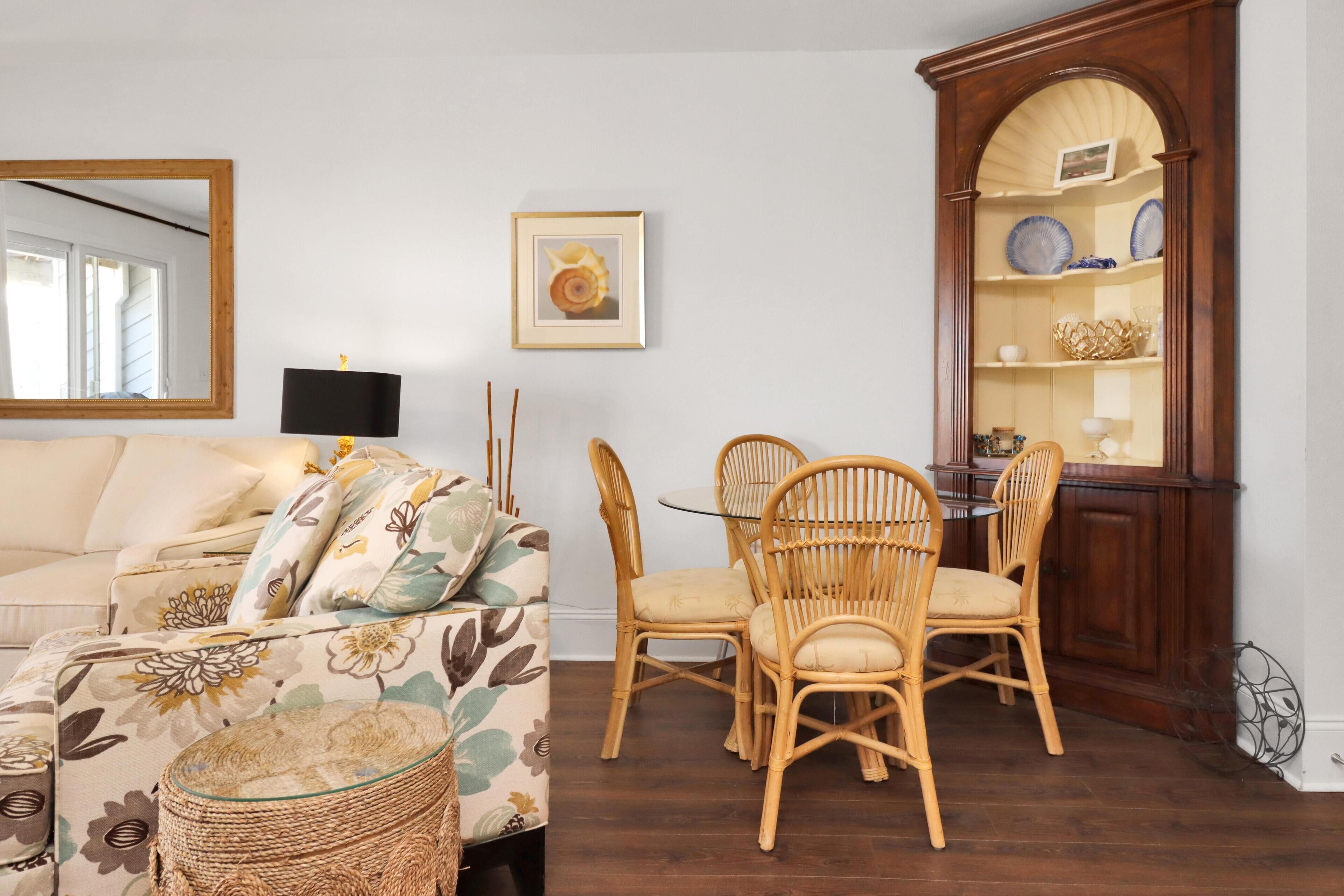 A living room with a sofa, chairs, a dining table, a mirror, and a wooden cabinet with shelves.