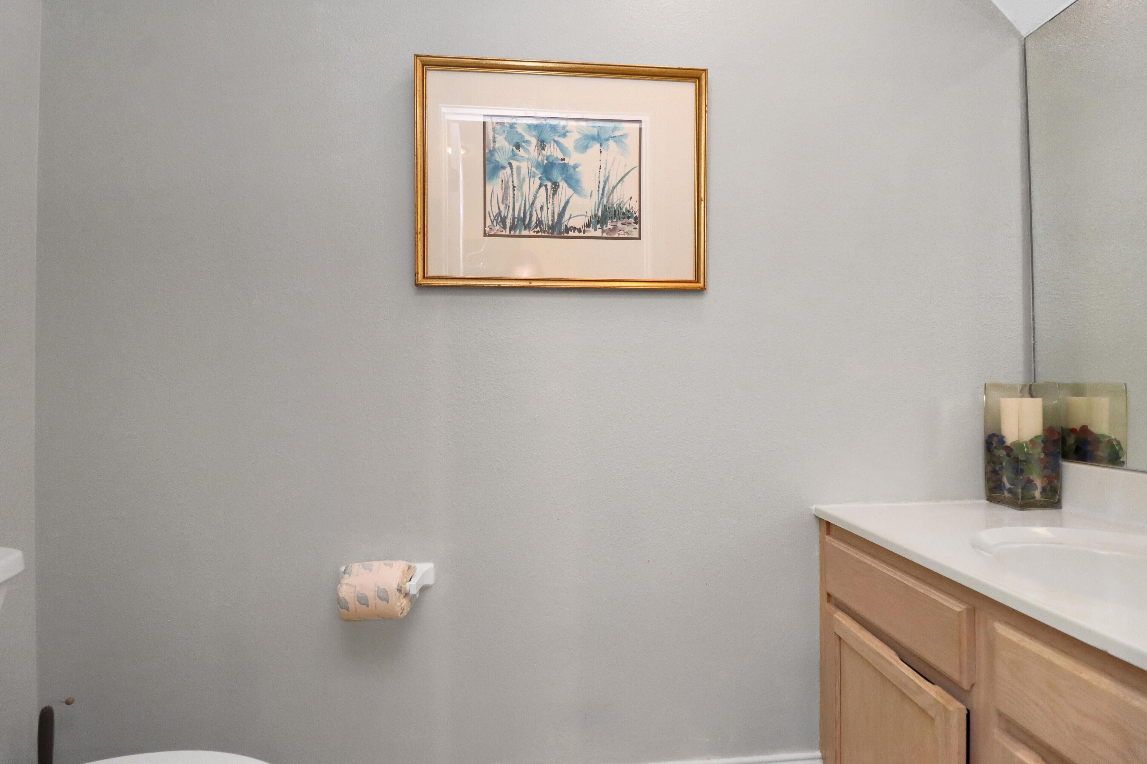 Een badkamer met een toilet, een wastafel, een spiegel en een lijst met een afbeelding aan de muur.