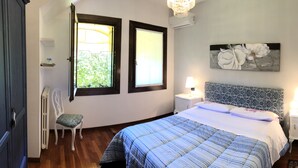 Une chambre à coucher avec un lit, deux lampes de chevet, une table de chevet, une chaise, une fenêtre et un tableau accroché au mur.