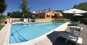 A swimming pool with lounge chairs and umbrellas, surrounded by a house and greenery.