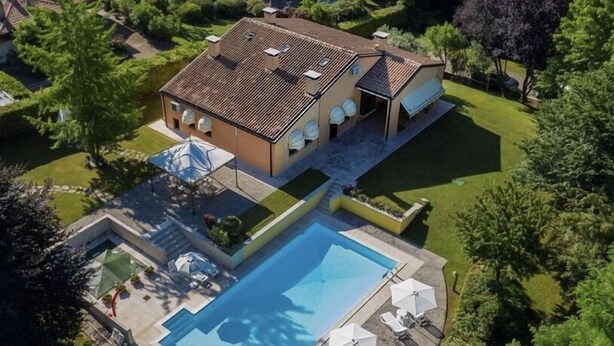 Une vue aérienne d’une maison avec une piscine, entourée de pelouses et d’arbres bien entretenus.