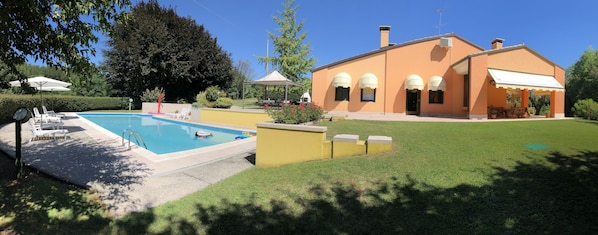 A pool with lounge chairs, a covered patio, and a building with arched windows and a white awning.