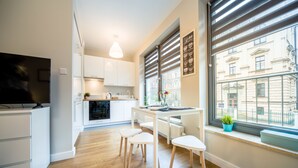Een moderne keuken met witte kasten, een eettafel met vier stoelen, een televisie en een raam met zonwering.