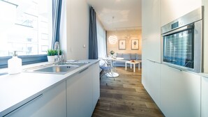 Een moderne keuken met een groot kookeiland, een inbouwoven en een eethoek met een ronde tafel en stoelen.