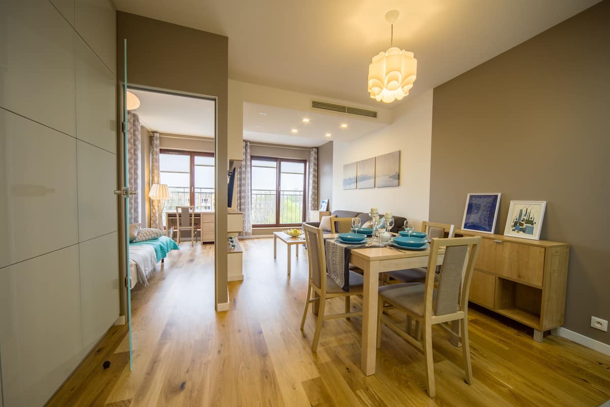 Un vaste espace de vie comprenant une table à manger pour quatre personnes, un canapé et une vue sur l’extérieur grâce à de grandes fenêtres.