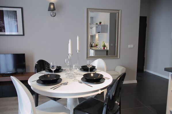 Un moderno comedor con una mesa redonda, sillas blancas, platos negros y un espejo grande en la pared.