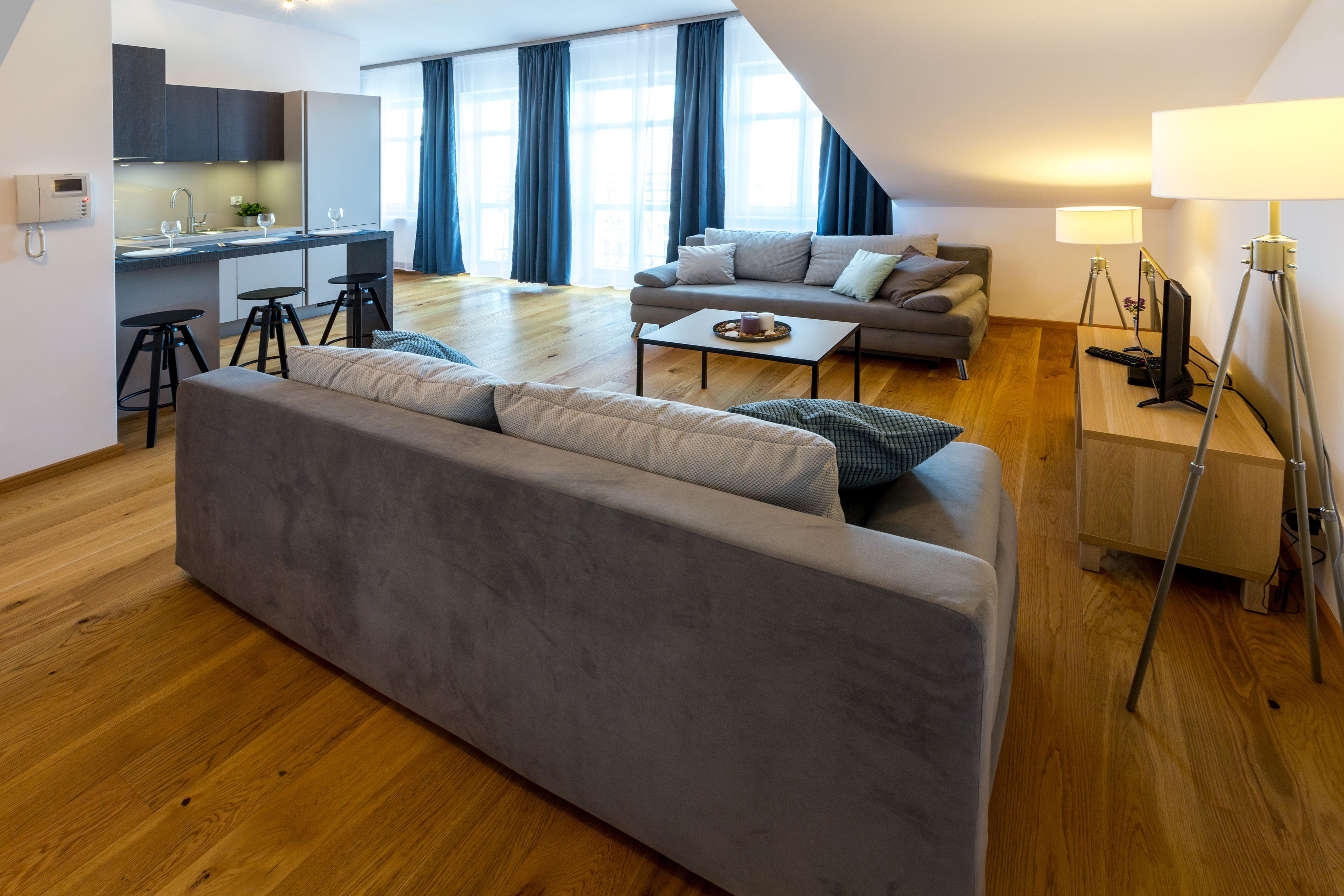 Un apartamento moderno con un sofá gris, una mesa de comedor y una zona de cocina.