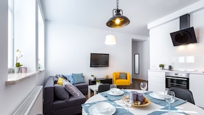 A modern living room with a sofa, dining table set for two, and a kitchen area with a TV and oven. - Friendhouse Apartments - Train Station Area (Kraków)