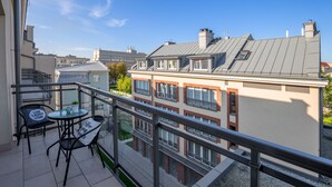 A balcony with a glass railing, two chairs, a small table, and a potted plant. - Friendhouse Apartments - Train Station Area (Kraków)